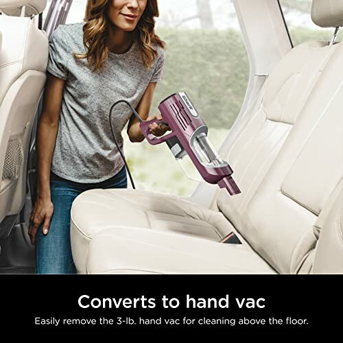 Person using a handheld vacuum cleaner inside a car.