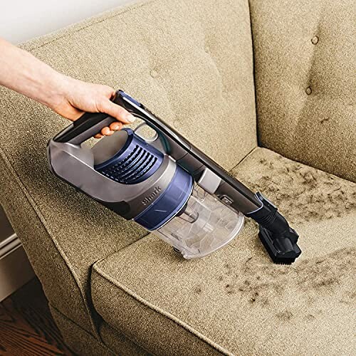 Person using a handheld vacuum cleaner on a sofa