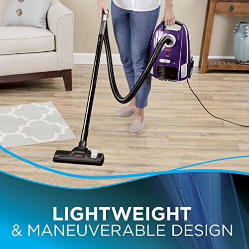 Person using a lightweight vacuum cleaner on a wooden floor.