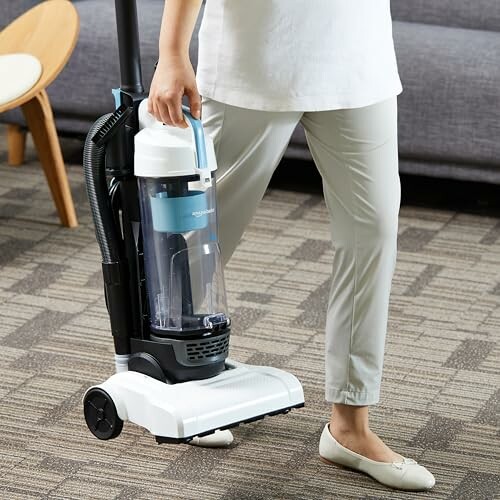 Person carrying an upright vacuum cleaner indoors.