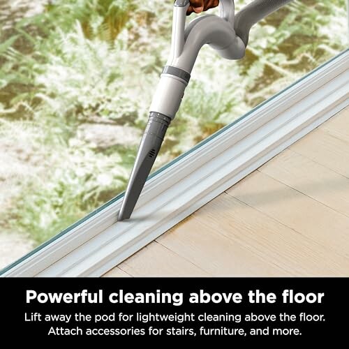 Vacuum cleaner being used on window track for above-floor cleaning.