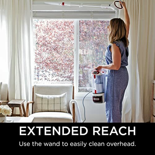 Person using a vacuum cleaner with extended wand to clean overhead.