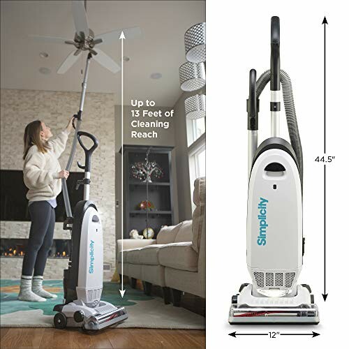 Person using a vacuum cleaner to clean a ceiling fan in a living room.