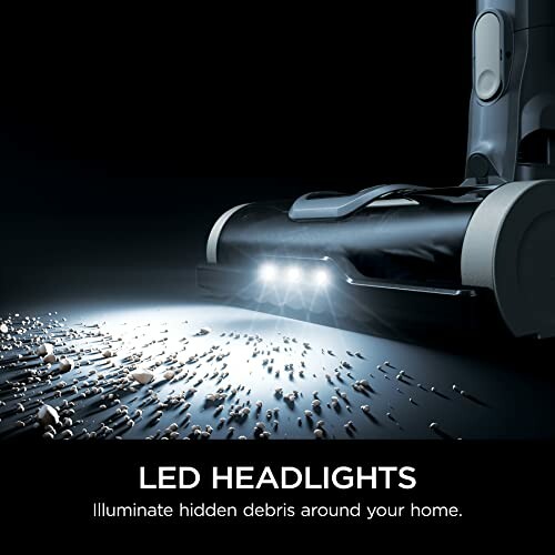 Vacuum cleaner with LED headlights illuminating debris.