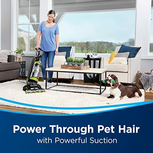 Person using vacuum cleaner with dog on rug, living room setting.