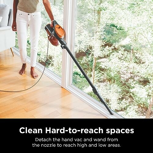 Person using a vacuum cleaner to clean hard-to-reach spaces by a large window.