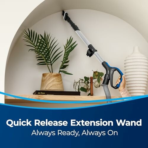 Person using a vacuum extension wand to clean a shelf with plants and books.