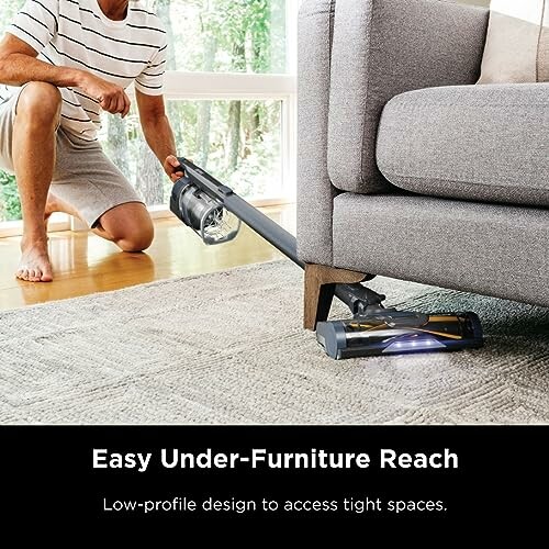 Person using a vacuum cleaner to reach under a couch.