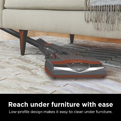 Vacuum cleaner reaching under a couch on a carpet.