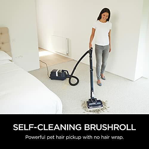 Woman using a vacuum cleaner with self-cleaning brushroll on bedroom carpet.