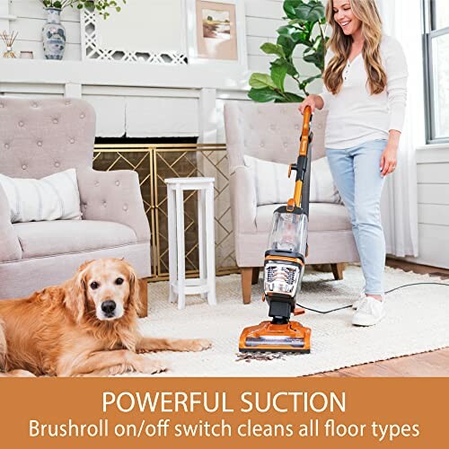 Woman using vacuum cleaner on carpet next to a dog in living room.